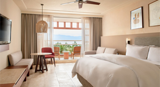 Interior view of the Ocean-View Junior Suite with a single king bed overlooking the trees and ocean.